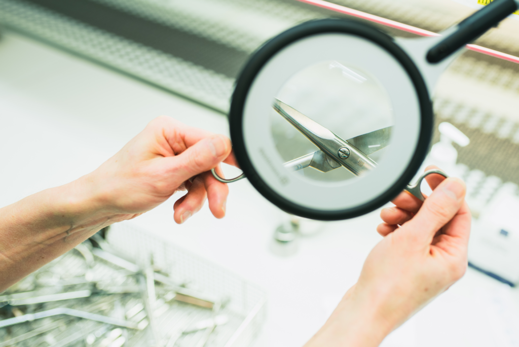 Kädessä olevia saksia katsotaan suurennuslasin läpi.